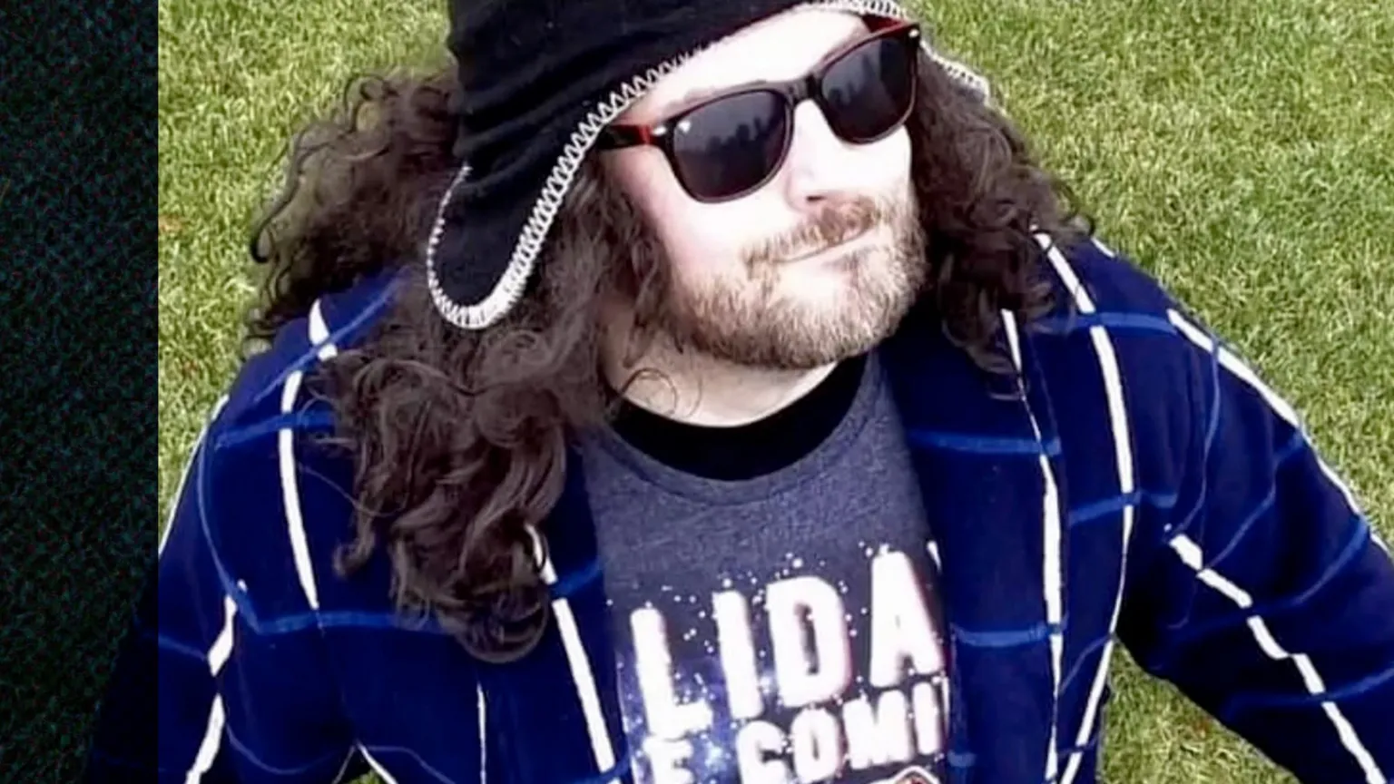 Stephen McCullagh wearing a blue and white jacket, dark sunglasses, a long black wig, and a black hat with ear covers.