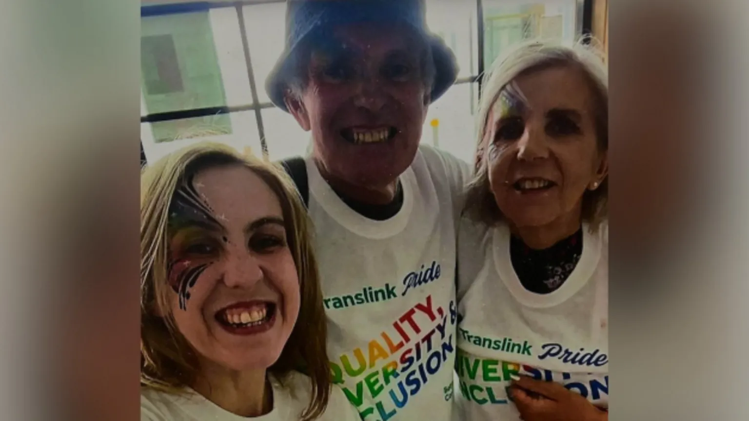 Family handout Natalie McNally smiling at the camera with her parents Noel and Bernie McNally. All three are wearing white Translink Pride t-shirts with a rainbow coloured logo which reads: 