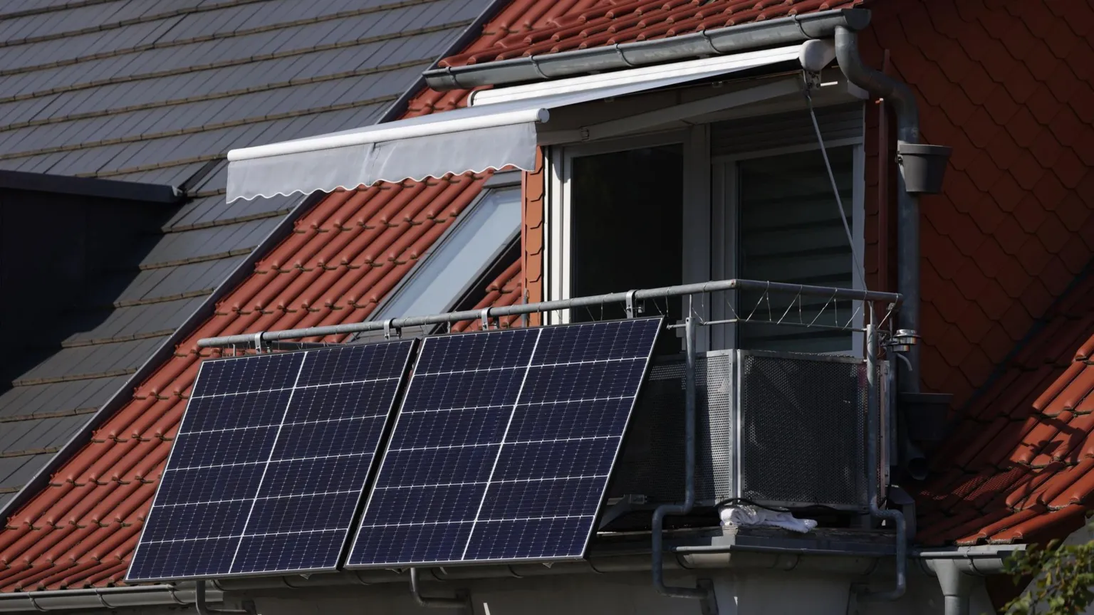 Sean Gallup/ Two small solar panels are shown hanging from a balcony in Germany, there is a red tiled roof to the left. 