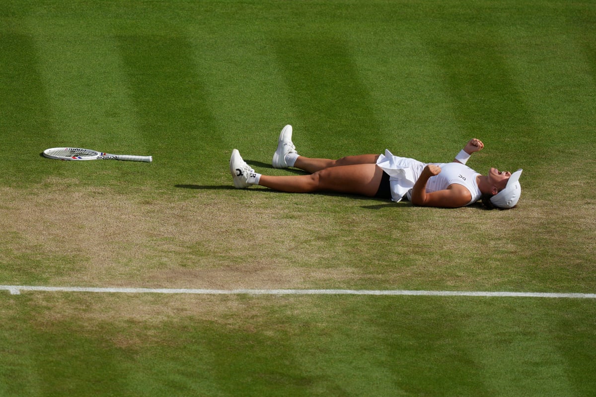 Iga Swiatek lies on the grass at Wimbledon with her fists clenched in celebration 