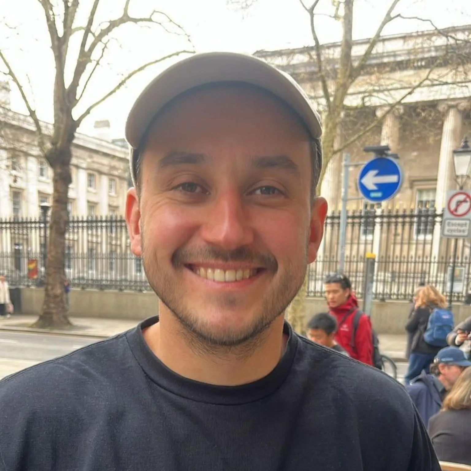 Selfie of young man in navy T-shirt, wearing a beige baseball cap. He's smiling at the camera. 