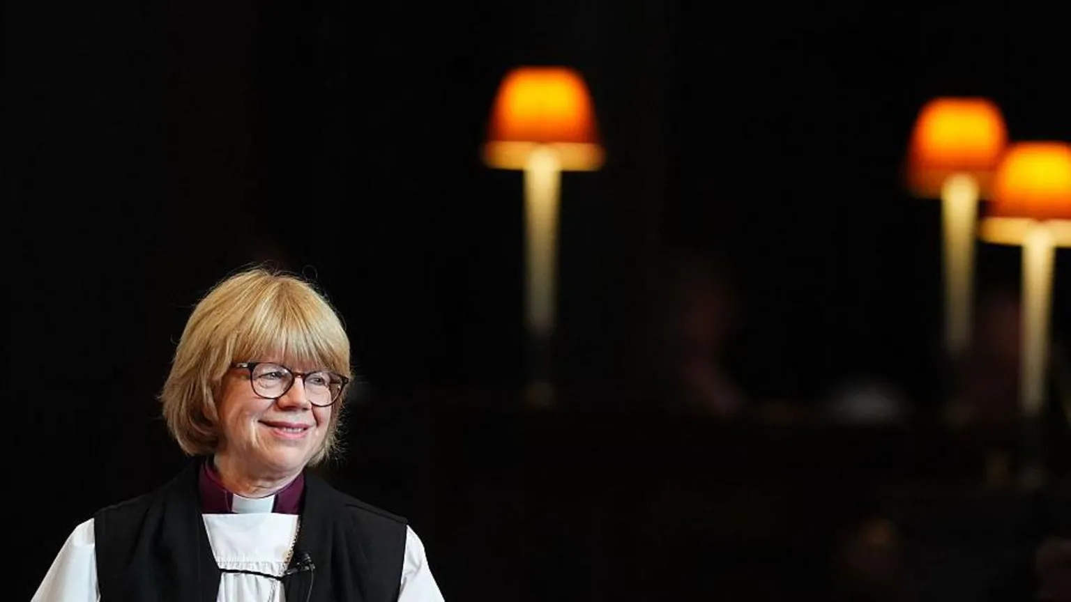 AFP via Sarah Mullally is pictured during the Confirmation of Election ceremony to legally confirm her position as the new Archbishop of Canterbury, at St Paul's Cathedral in London on January 28, 2026. She is smiling has her head turned to the side. He is wearing church robes. Lights can be seen in the background.