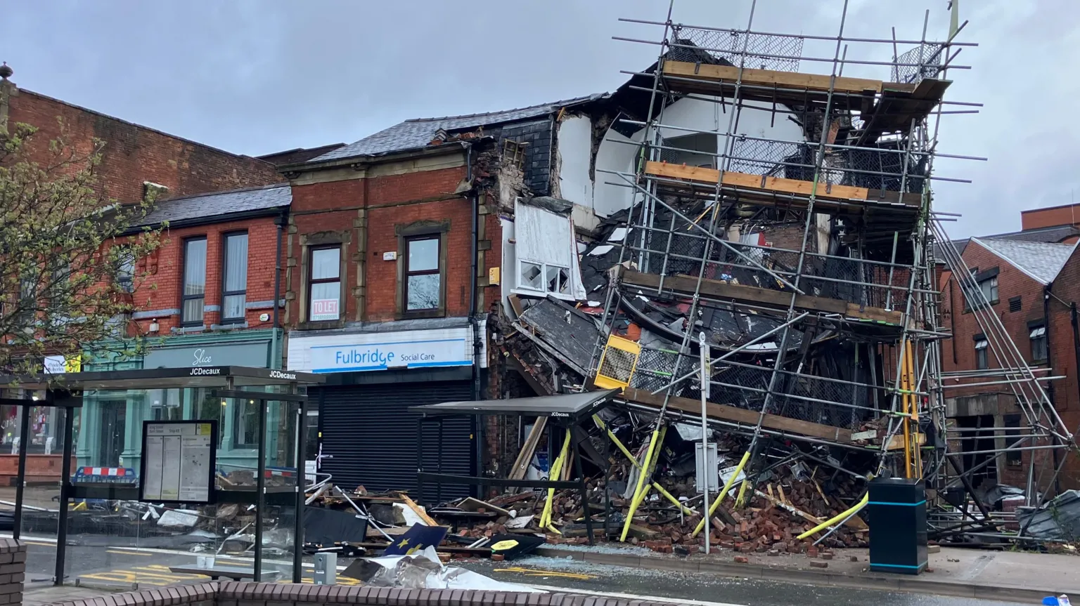 Mat Trewern/BBC Debris and a smashed bus stop are in front of a partially collapsed building with scaffolding dangling from it.