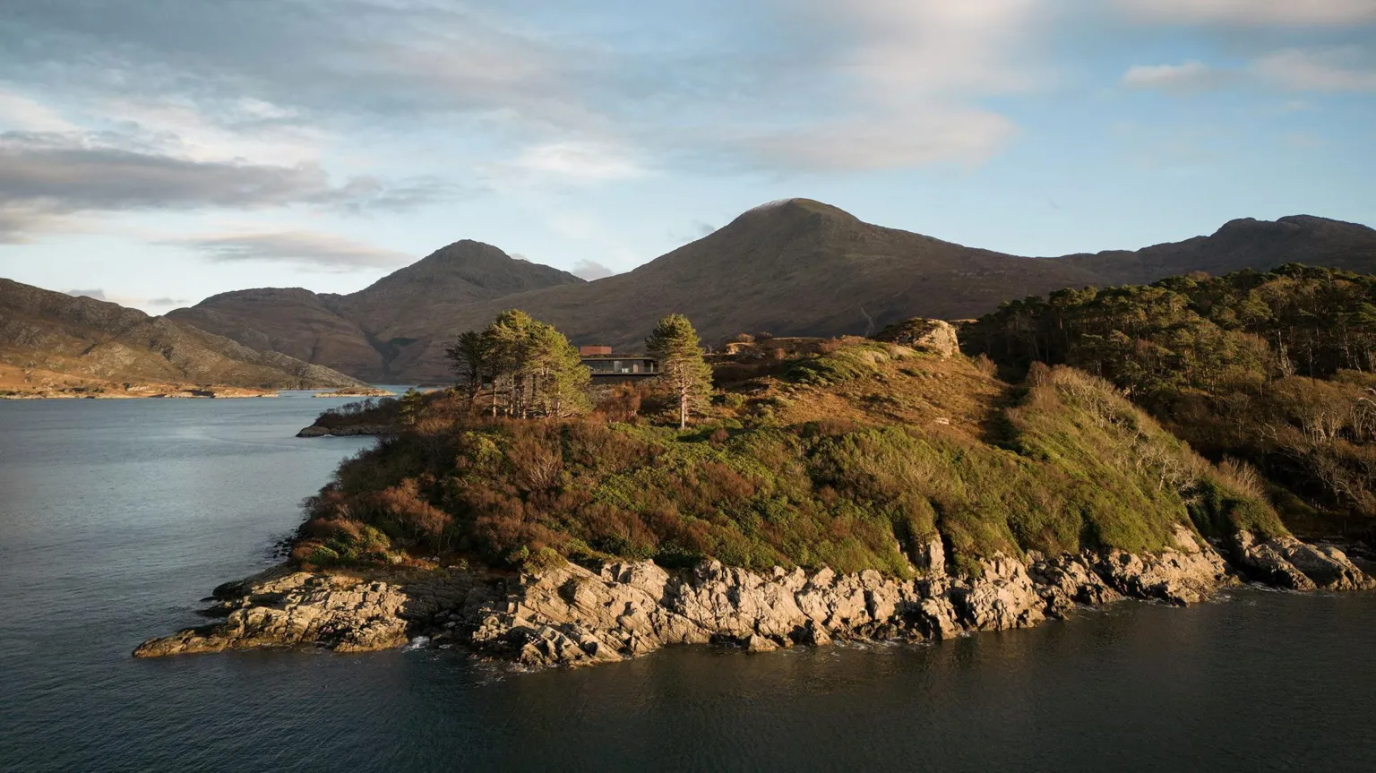 Brown & Brown Architects A drone view of the site, a rocky shoreline on the loch with hills in the background.