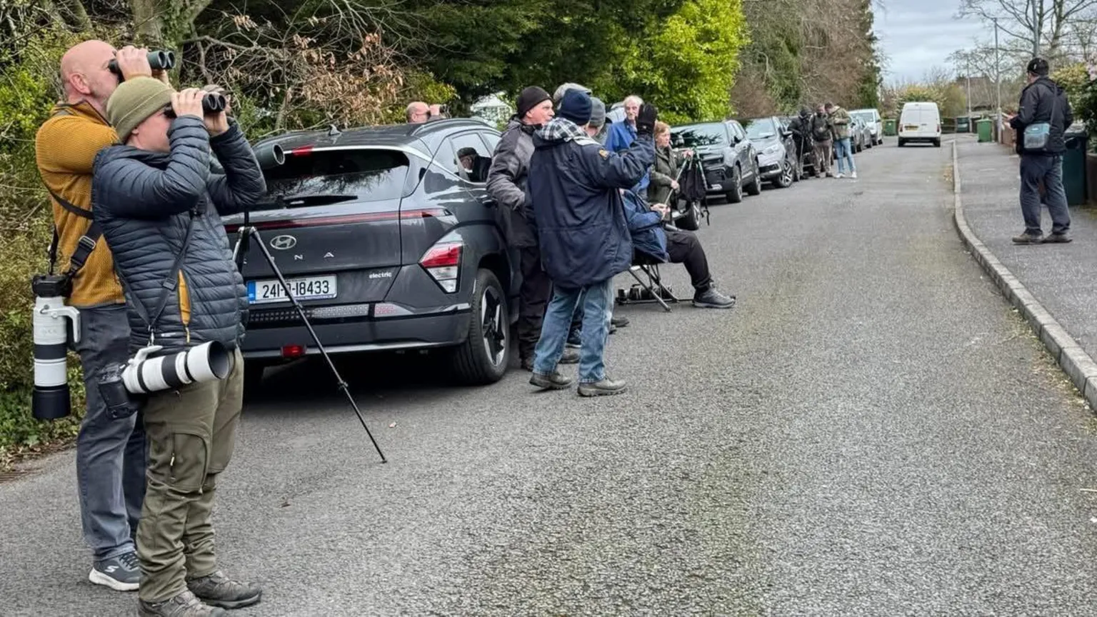 Garry Wilkinson People and cars lined along the road, people have cameras and are looking through binoculars