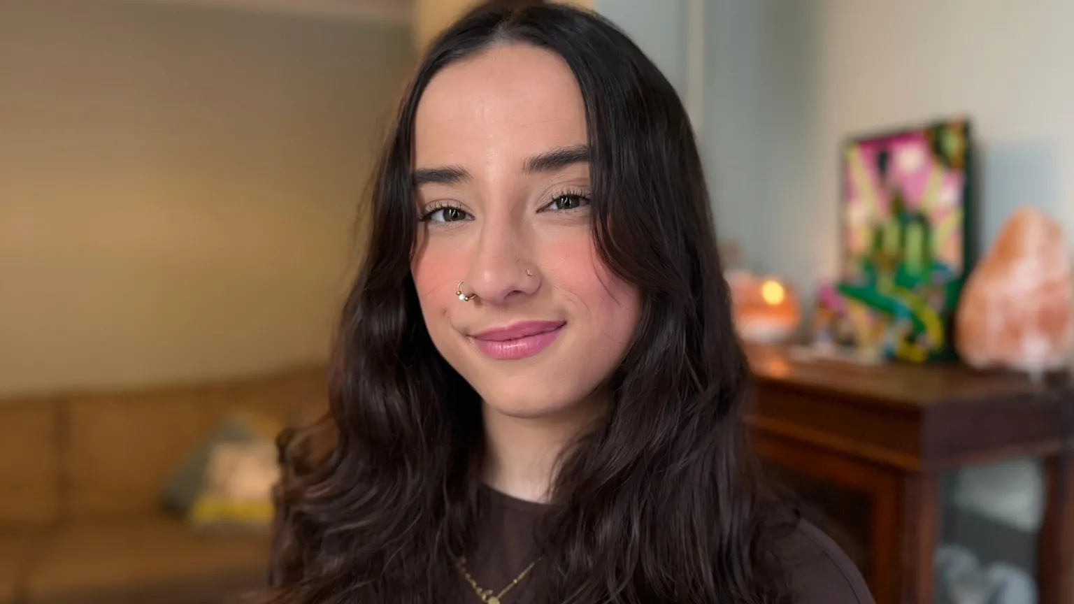 Yolanda Shirin/BBC A woman with brunette hair is in the centre of the photograph. The blurred background shows a sofa and a cabinet with artwork on top.
