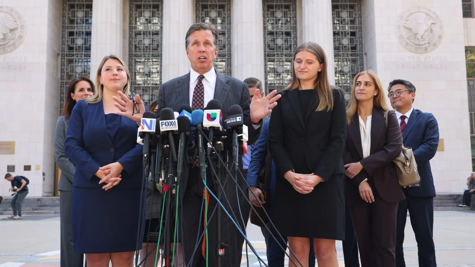 EPA A lawyer dressed in a grey suit speaks into a bunch of microphones with his hands out in front of him, as a group of people dressed in dress suits gather around him outside the front of a courthouse.