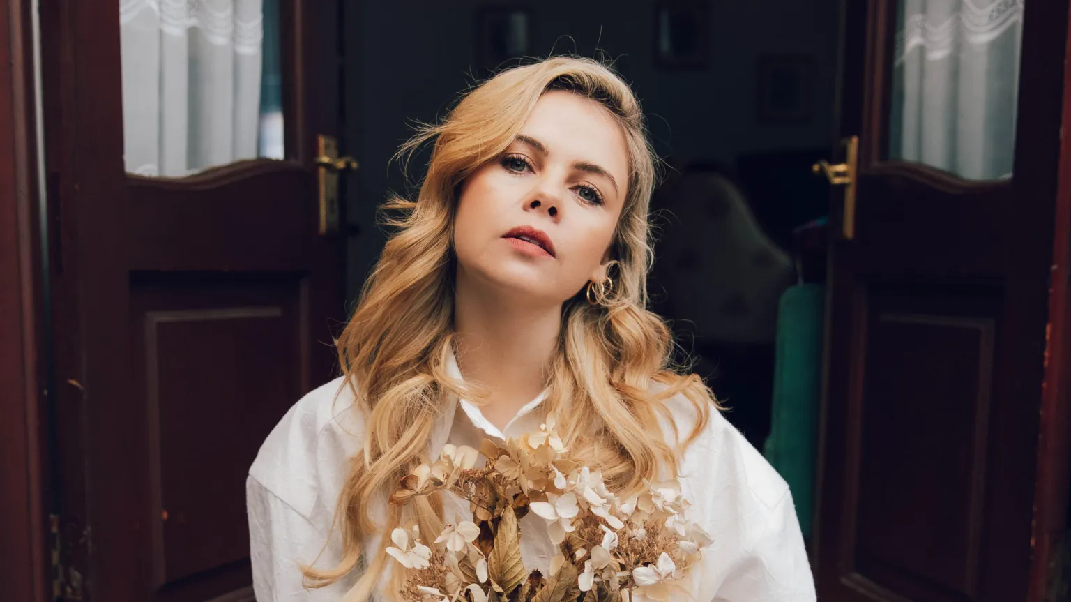 Bryony Coles Saoirse-Monica Jackson has long blonde curly hair. She is wearing a flowing white blouse.