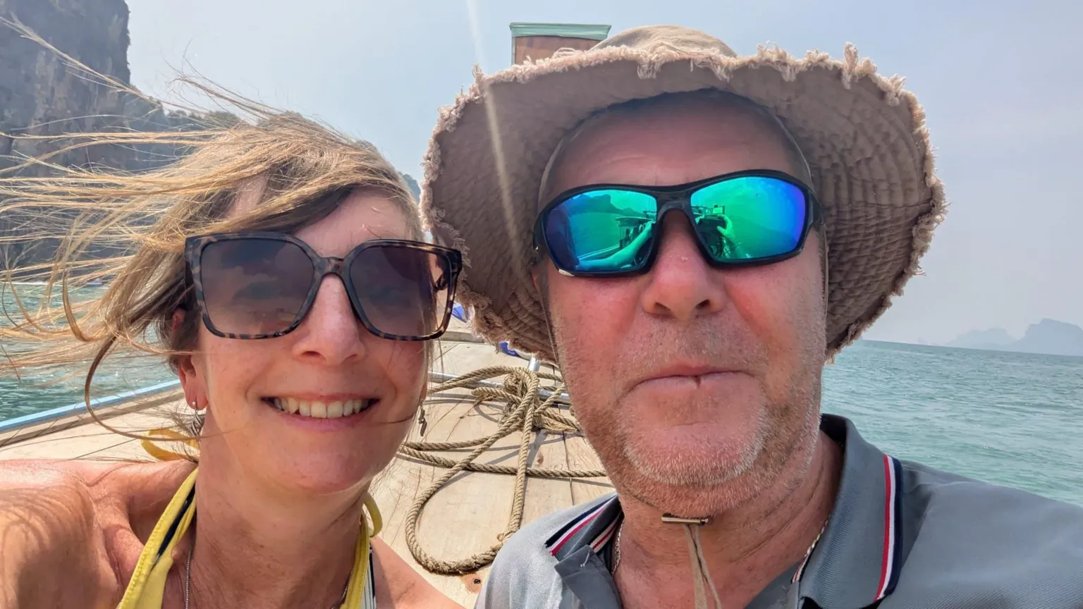 Supplied A man and a woman in a head and shoulders selfie on a boat. She is to the left and has windswept brown hair, sunglasses and the straps of a yellow halterneck top. He is wearing sunglasses, a grey top and brown hat. Behind them is a sunny backdrop of a blue ocean.