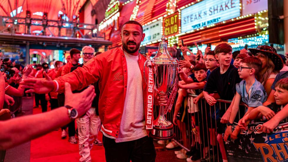 Hull KR captain Elliot Minchella claps hands with fans as he walks down the Fremont Street rugby league takeover walkway, clutching the World Club Challenge trophy in his other hand
