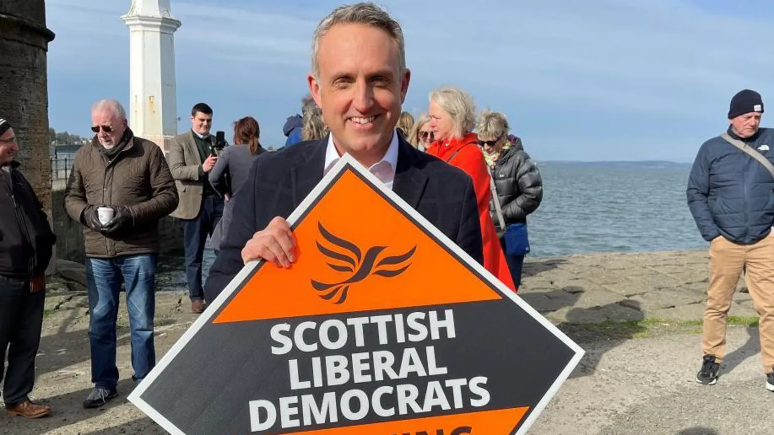 Man on beachfront holding political banner reading 