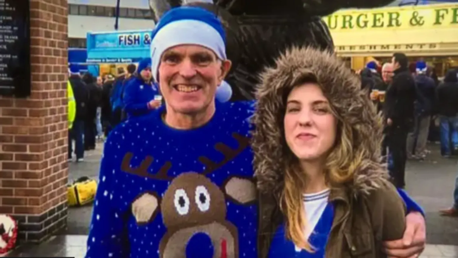Family handout A man and woman stand outside a football ground on a wet day. The man, Noel McNally, is wearing a blue Christmas jumper with a large reindeer motif and a blue and white hat. The woman, his daughter Natalie McNally, is wearing a blue and white football jersey under a brown overcoat with a brown fur hood. Her father's hand is placed around her shoulder.