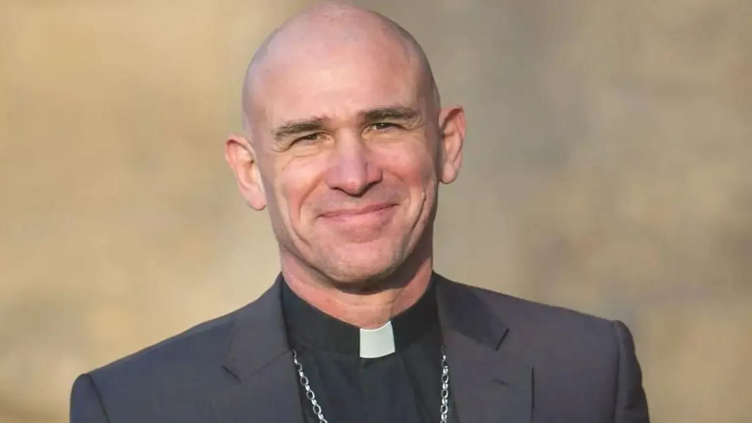 Church of England A bald man is smiling and wearing a black jacket and black shirt with a clerical collar.