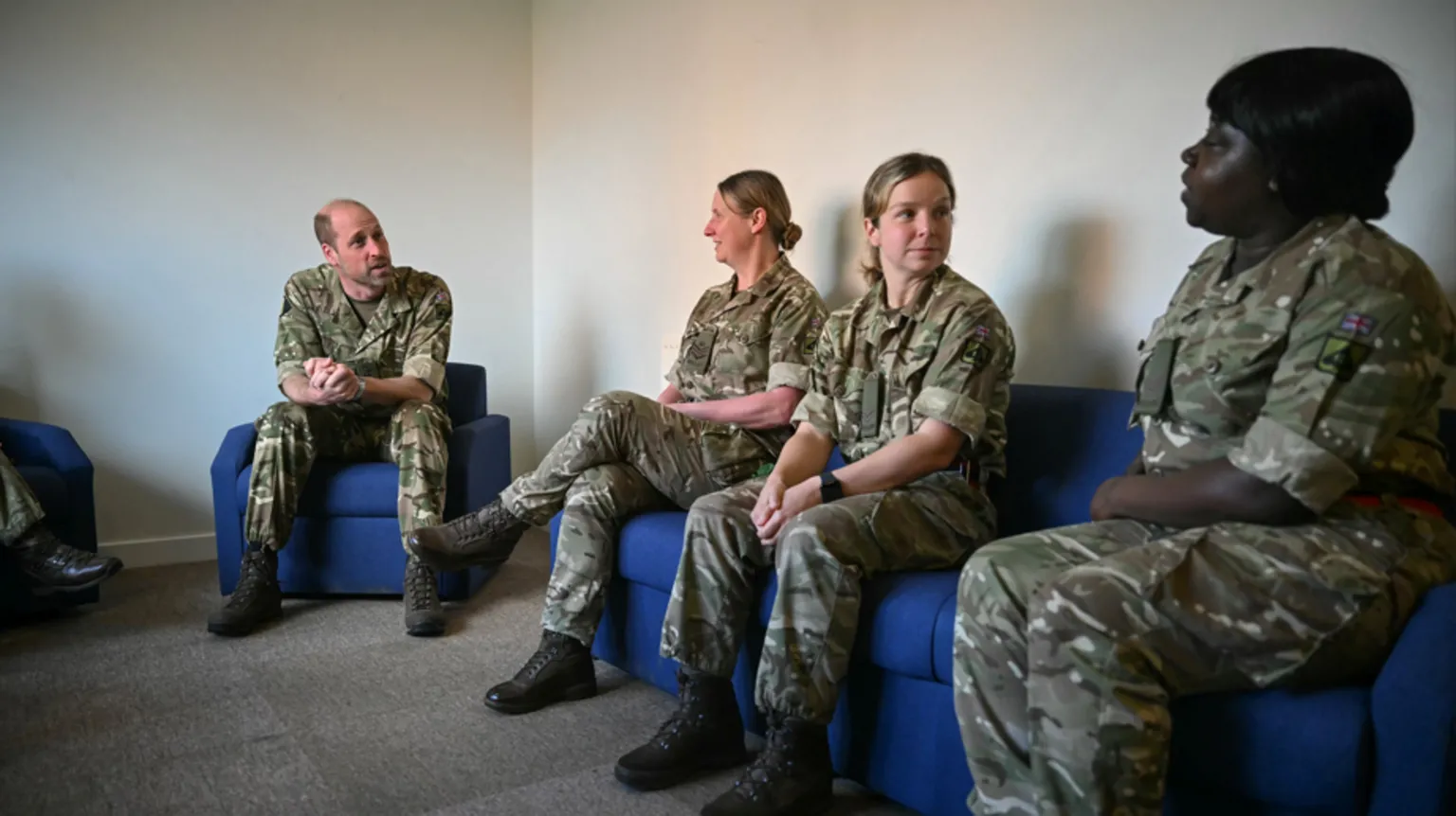 Justin Tallis/PA Wire Prince William, in his camouflage gear, sits on blue chair and speaks to women in military attire.