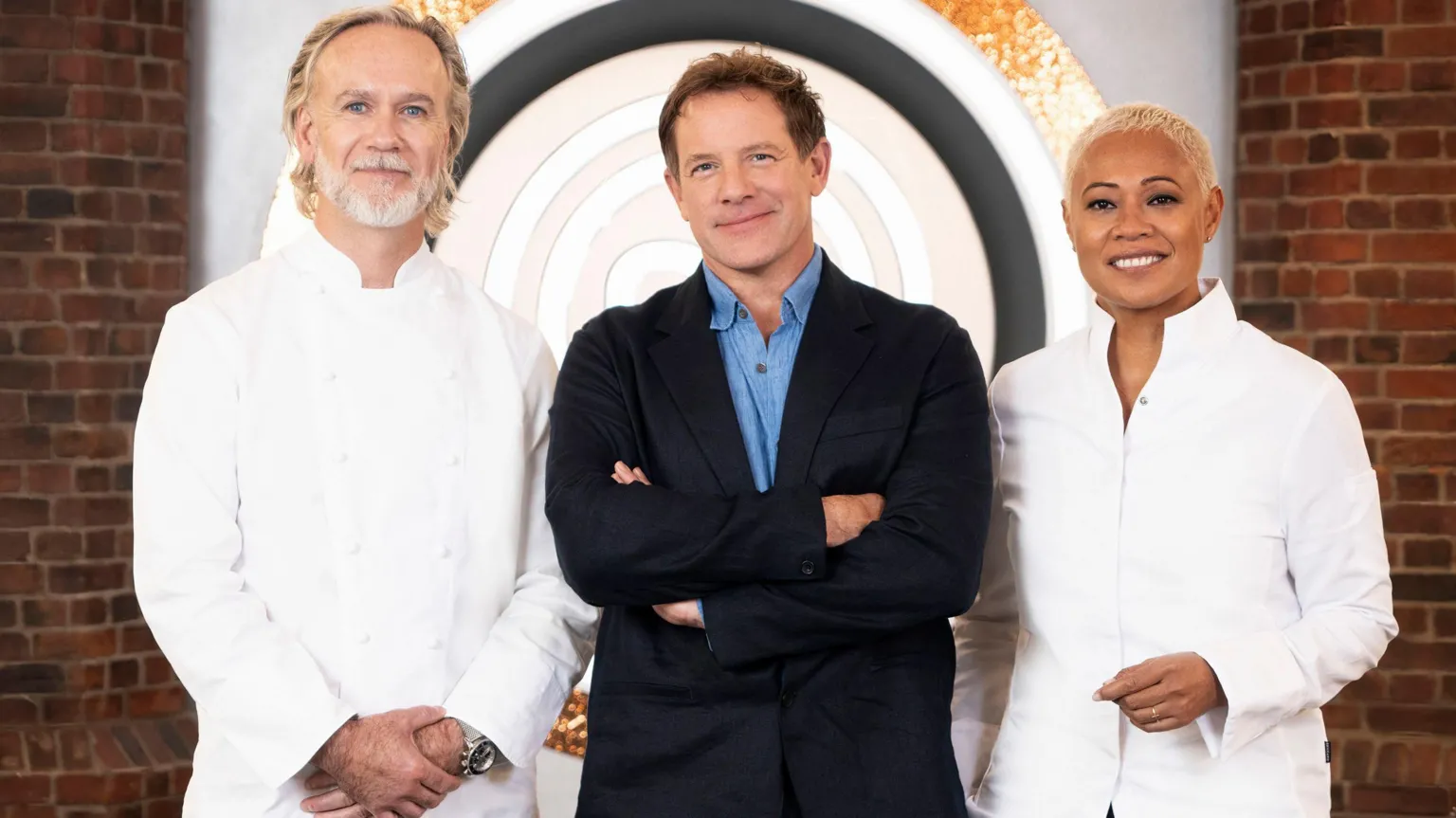 BBC/Shine TV The three judges of series 18 of MasterChef The Professionals on the set of the show. Marcus Wareing and Monica Galetti wear chefs coats and black trousers, with Matt Tebbutt standing between them, wearing a navy suit with blue shirt. Wareing has long blond hair combed back, blue eyes and a trimmed white beard. Waring has short brown hair and blue eyes. Galetti has blond short hair. The three are standing on set and smiling