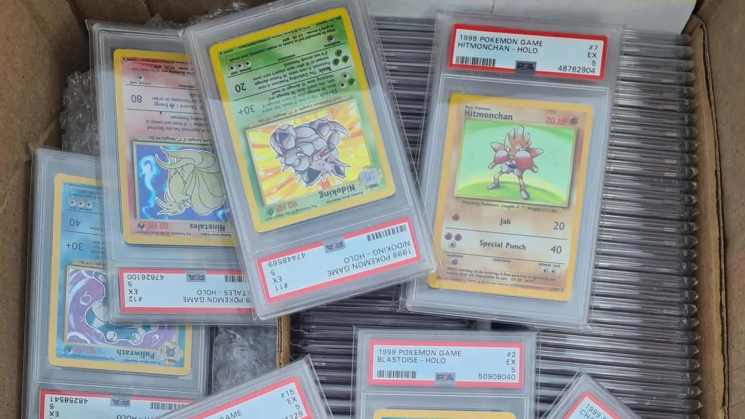 Barry Lloyd A few scattered PSA graded Pokémon cards laid on top of a densely-packed row of them beneath. All put in a brown cardboard box. 