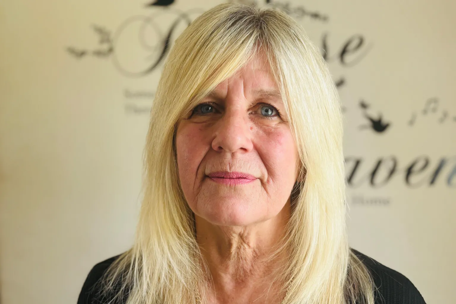 Caroline Munro, a woman with long blonde hair and a black top, smiling at the camera.