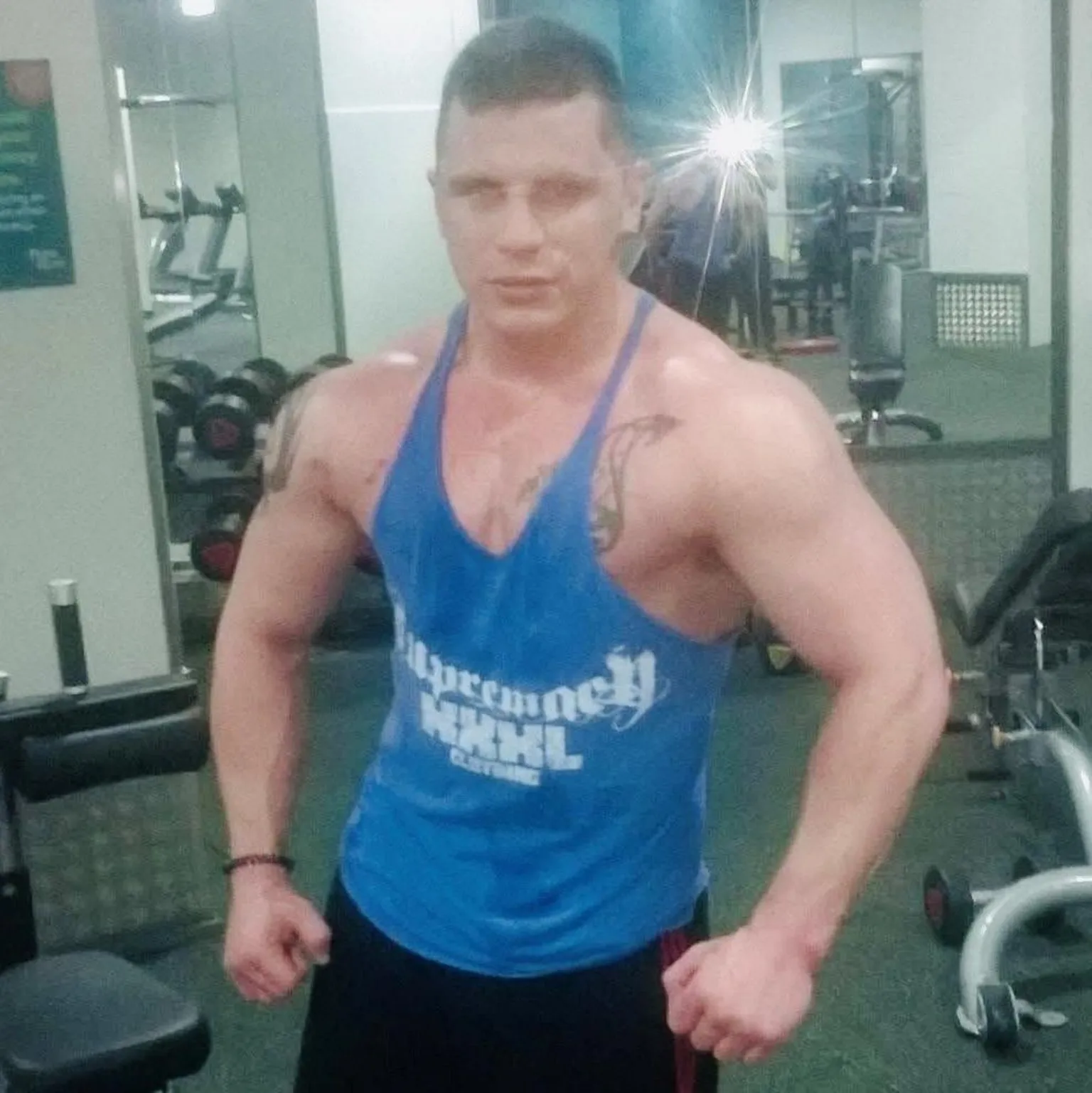 Caroline Munro Jordan Jones pictures flexing his muscles in a gym, he is wearing a blue vest top, and gym equipment is behind him.