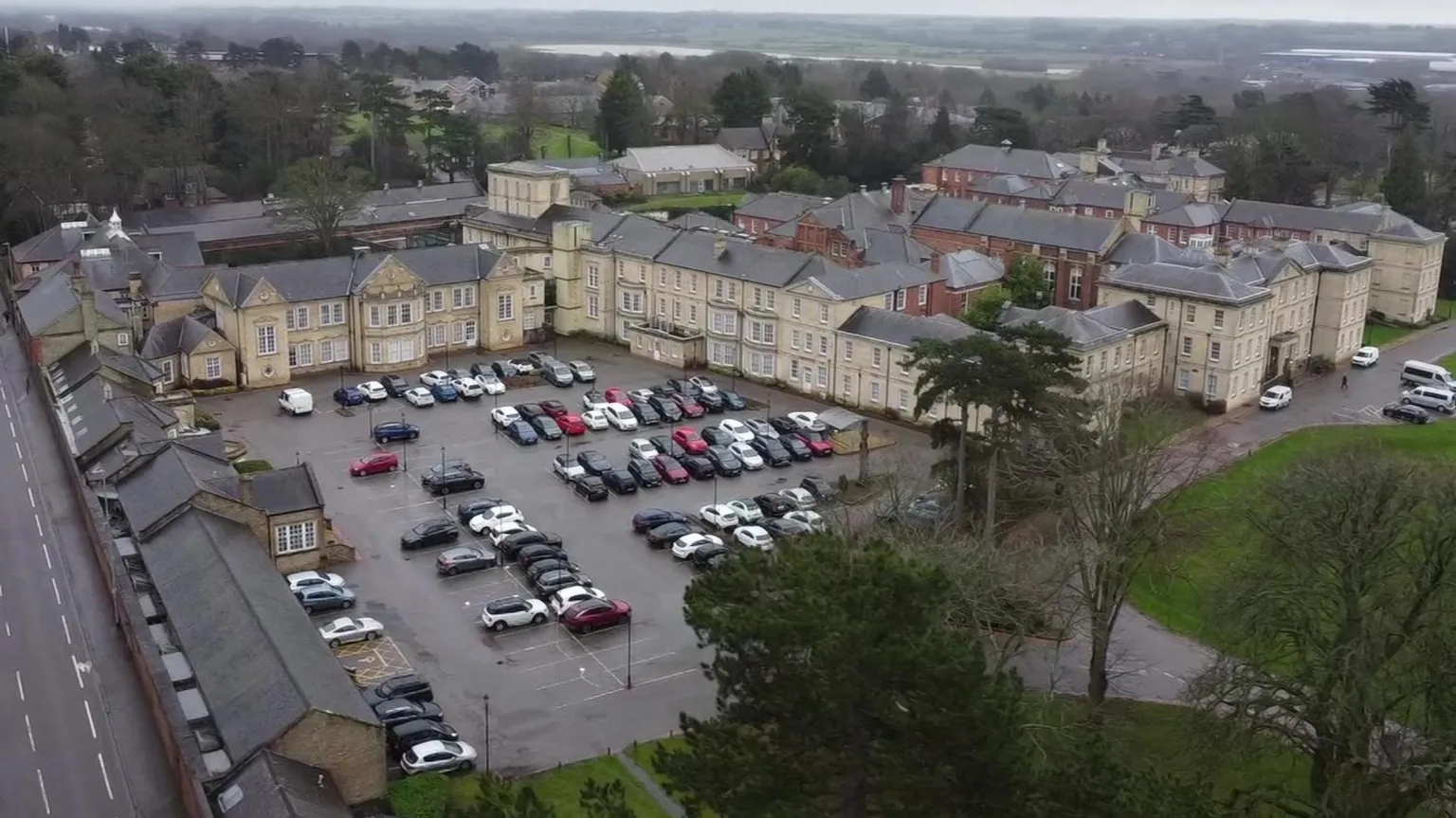 Dawid Wojtowicz Aerial pictures of a large hospital site. There are numerous buildings which are attached or contiguous to one another. The buildings are coloured off-white or a shade of orange-red. There is a car park. To the left of the picture is a busy road.
