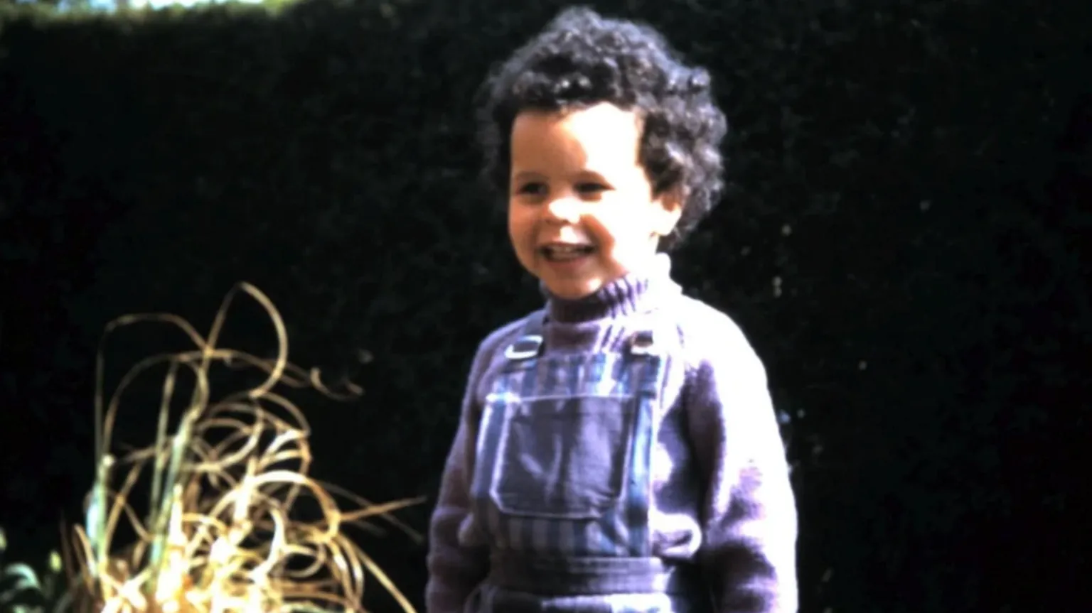Vik Fielder Fielder as a young girl, with short black curly hair and wearing a purple jumper and blue, striped dungarees.