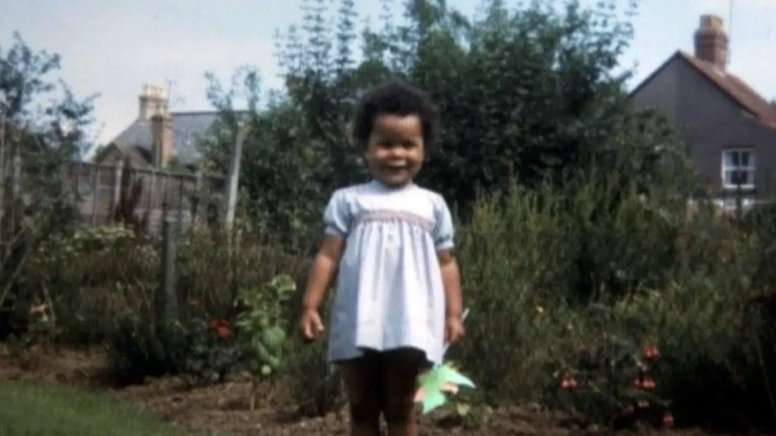 Vik Fielder Vik Fielder standing in a garden as a young girl, wearing a dress and smiling. She has short black hair and is holding a windmill toy.