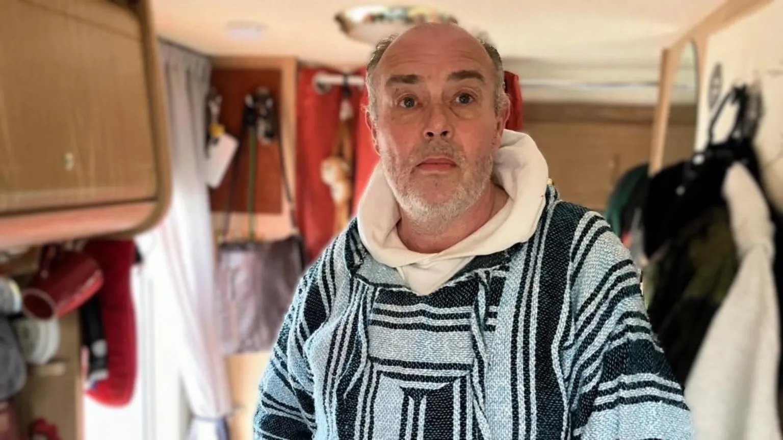 BBC/Seb Cheer A man, Richard, stands in his campervan and looks into the camera with a neutral expression on his face.