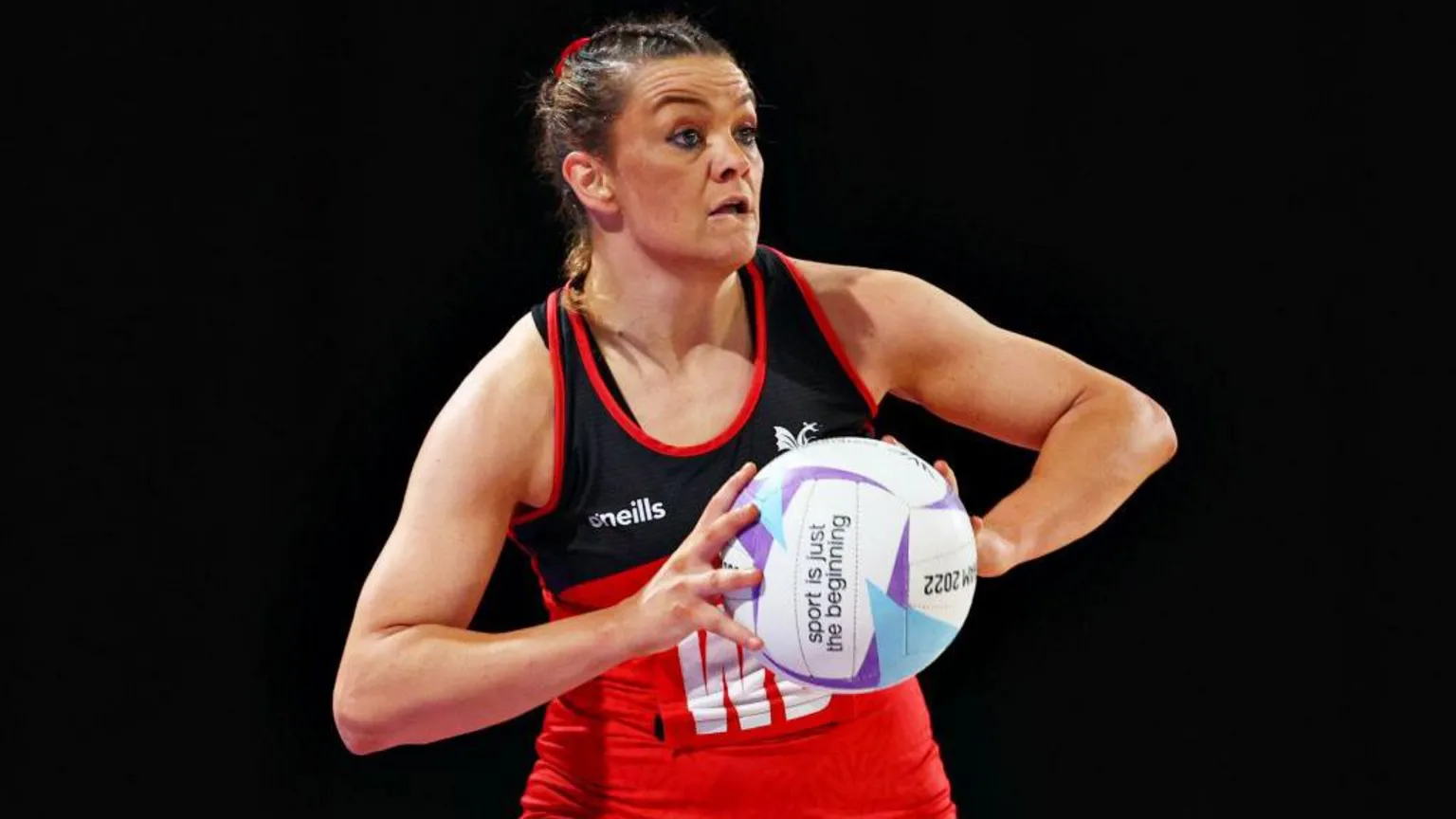  Close up of Nia Jones playing netball. She wears a Cardiff dragon netball dress and holds a ball in front of her with both arms. 
