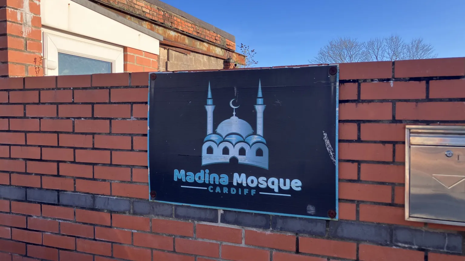 Sign for Madina Mosque on a low wall on the outside of the brick building in Cathays, Cardiff