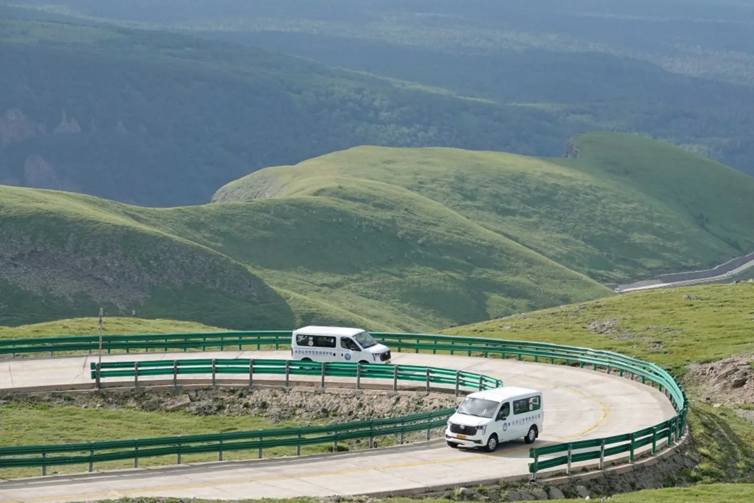 A hilly landscape with grassy mounds and a winding road with green crash barriers on the side of the road