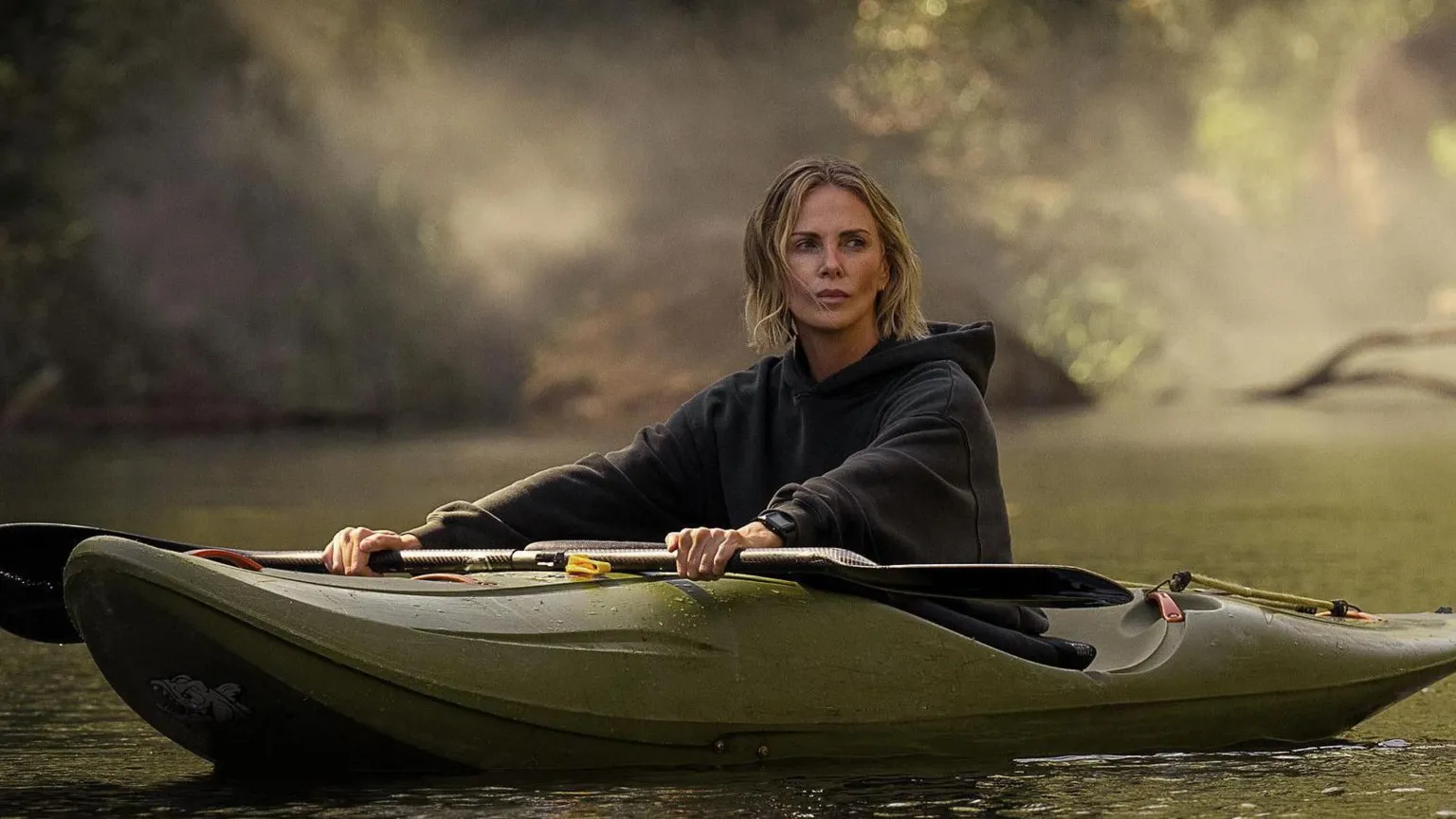 KANE SKENNAR/NETFLIX Theron sitting in a green canoe and wearing a grey hoodie. Her blonde hair is shoulder-length