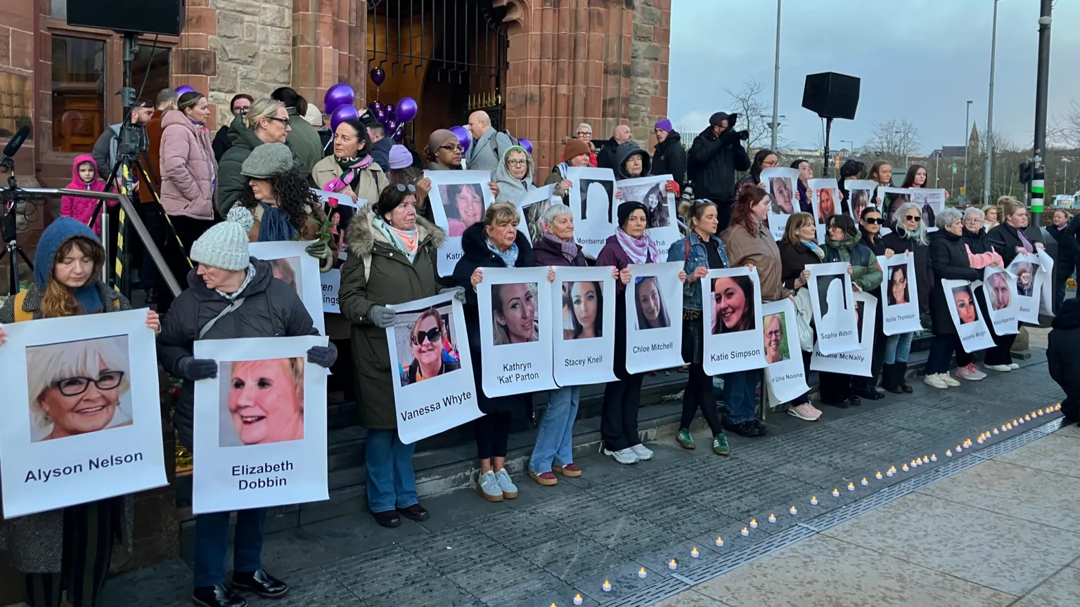 A group of women stand on the steps of Derry's Guildhall, each holding a poster of a woman killed in Northern Ireland