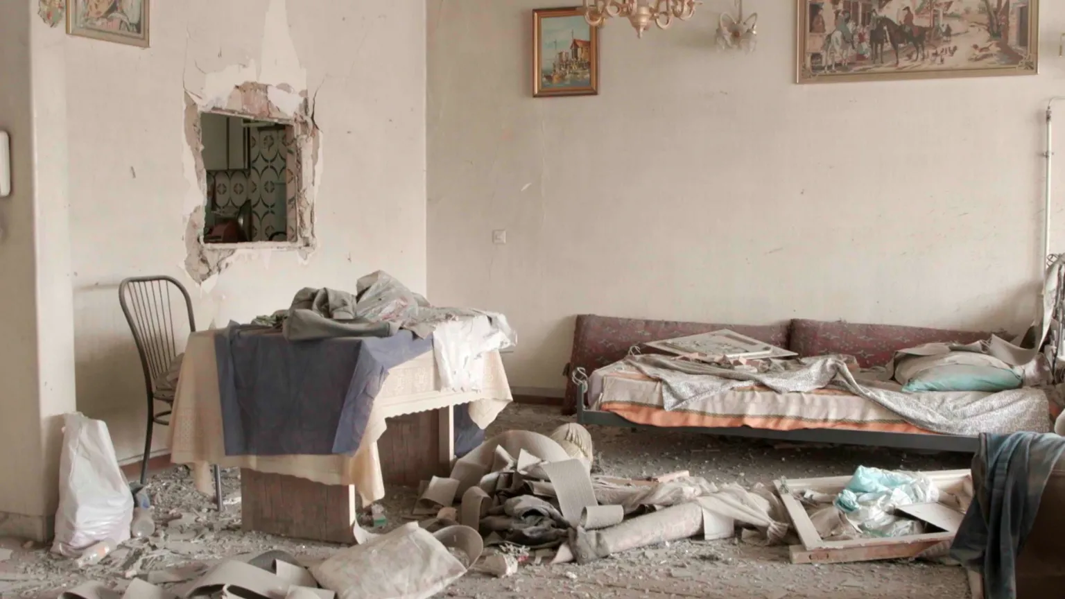 A photo shows the inside of a heavily damaged apartment, with rubble strewn across the fllor and a damaged sofa and table.