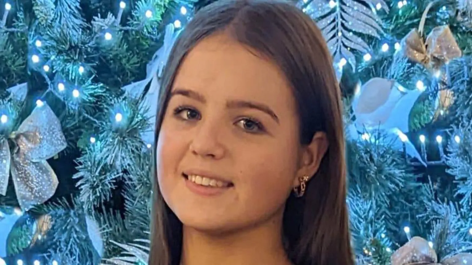 Bob Hogg A 13 year old girl stands in front of a Christmas tree. She is wearing a Kinawley Brian Borus football top, in navy and blue with a crest on the chest. She is smiling and has long dark hair and is wearing gold hoops in her ears. The Christmas tree is decked out in blue lights and pale gold decorations. 