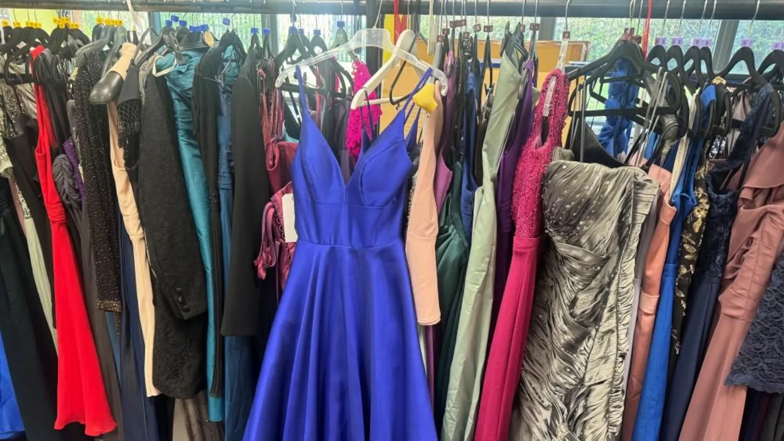 Annabel Amos/BBC A large row of prom dresses on a rack. A blue dress is hung the other way on the rack, so it is straight on. The dresses are all in all different shapes and sizes