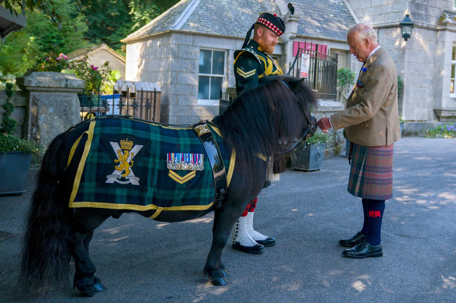  King Charles III meets Shetland pony Cpl Cruachan IV (mascot of the Royal Regiment of Scotland) during an inspection of the Balaklava Company, 5th Battalion, The Royal Regiment of Scotland, at the gates of Balmoral. The King is wearing a kilt and a light brown jacket.