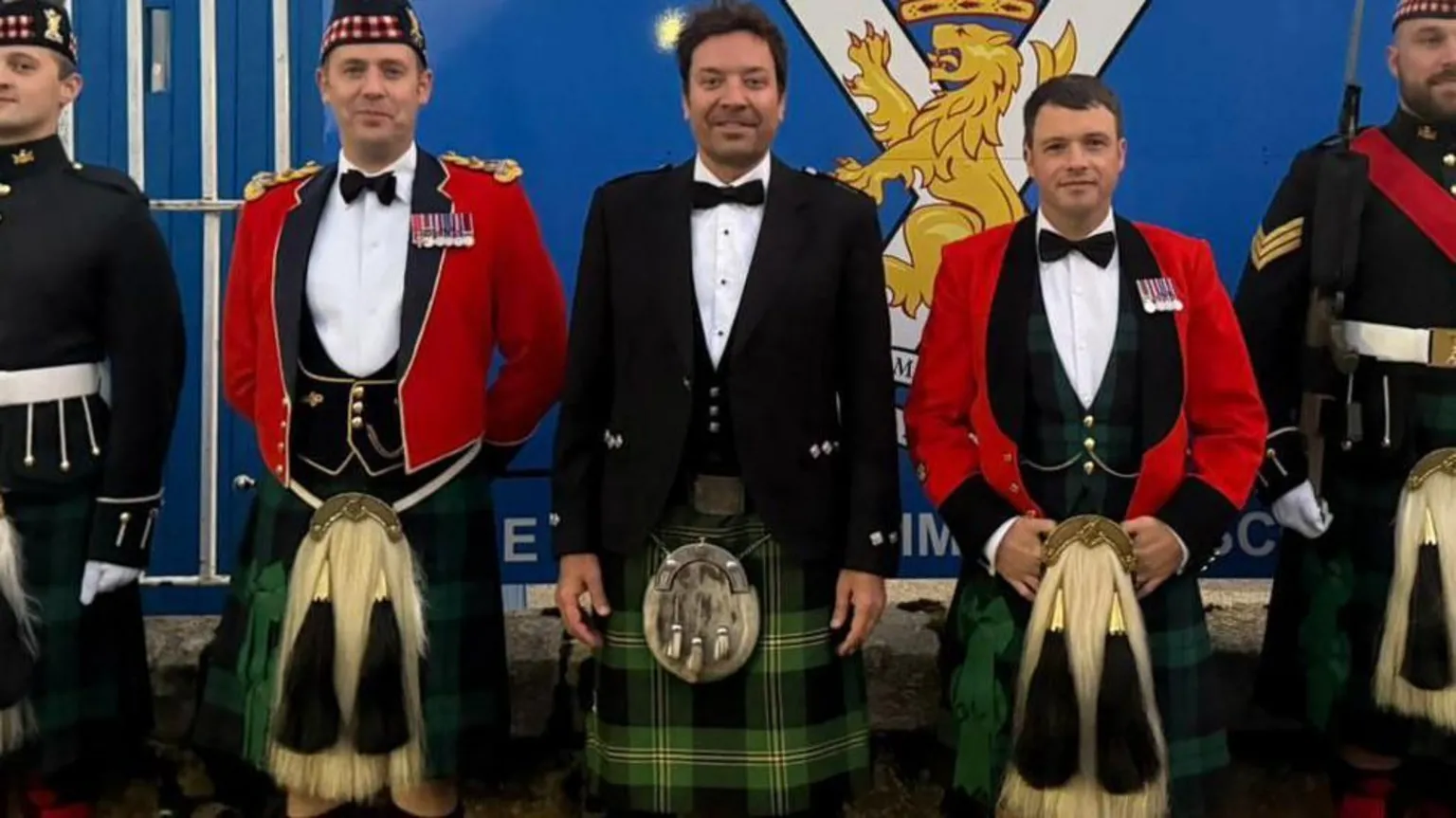  A row of men, including Jimmy Fallon, wearing kilts standing in front of a sign which reads 'His Majesty the King's Royal Guard'.