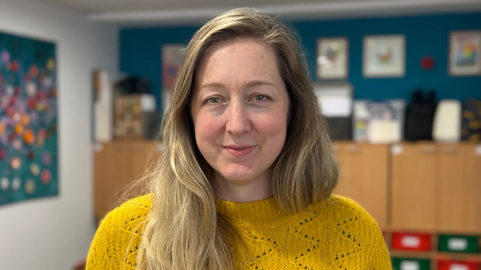 Steph is looking to camera and is wearing a yellow jumper.