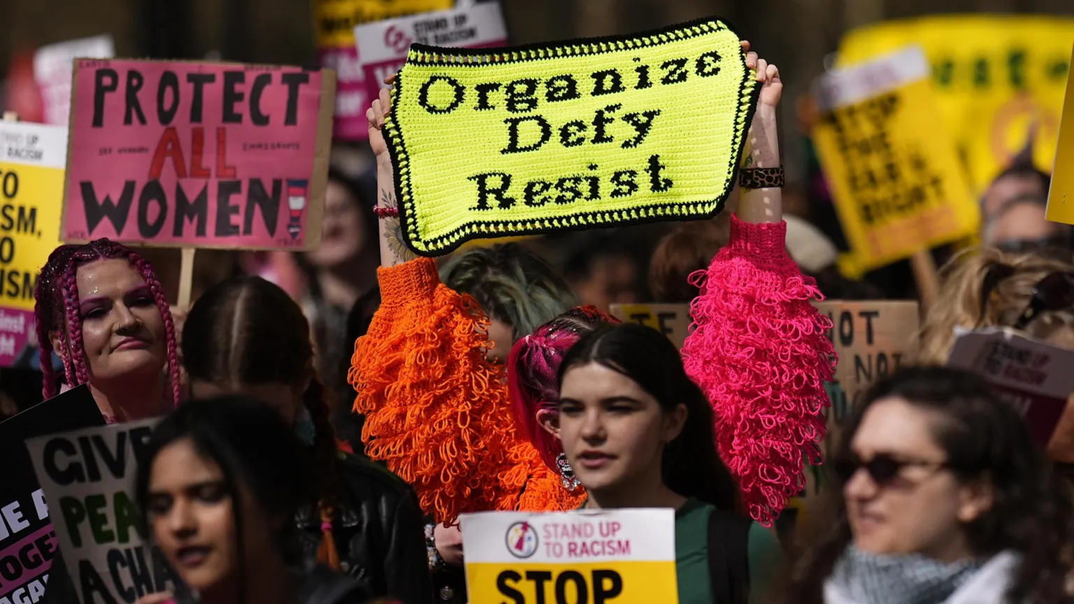 PA A group of women holding up signs at a rally. one of the signs his crocheted and reads organise, defy, resist.