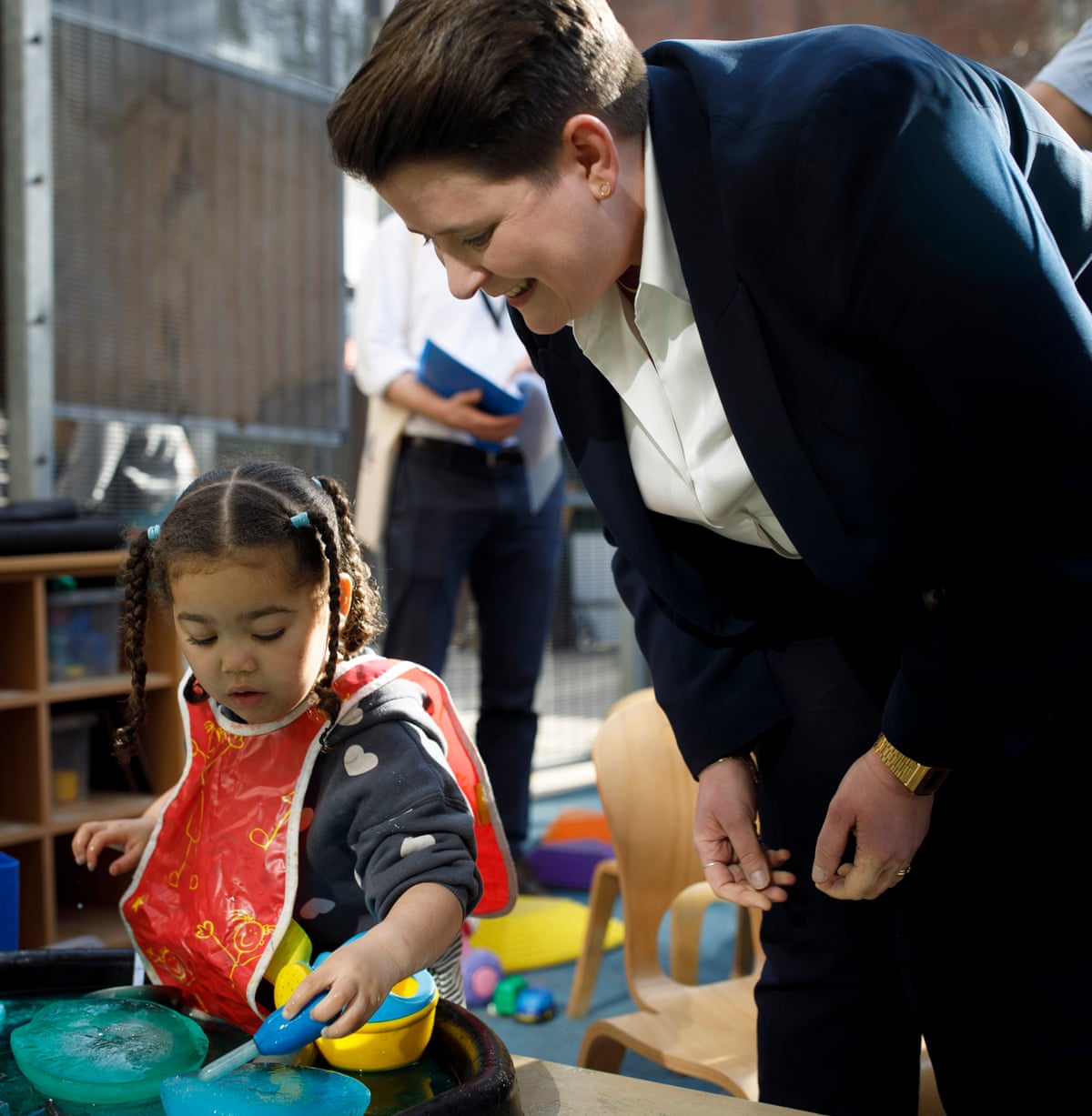 Olivia Bailey smiles and looks on as a young girl plays with toys at the centre