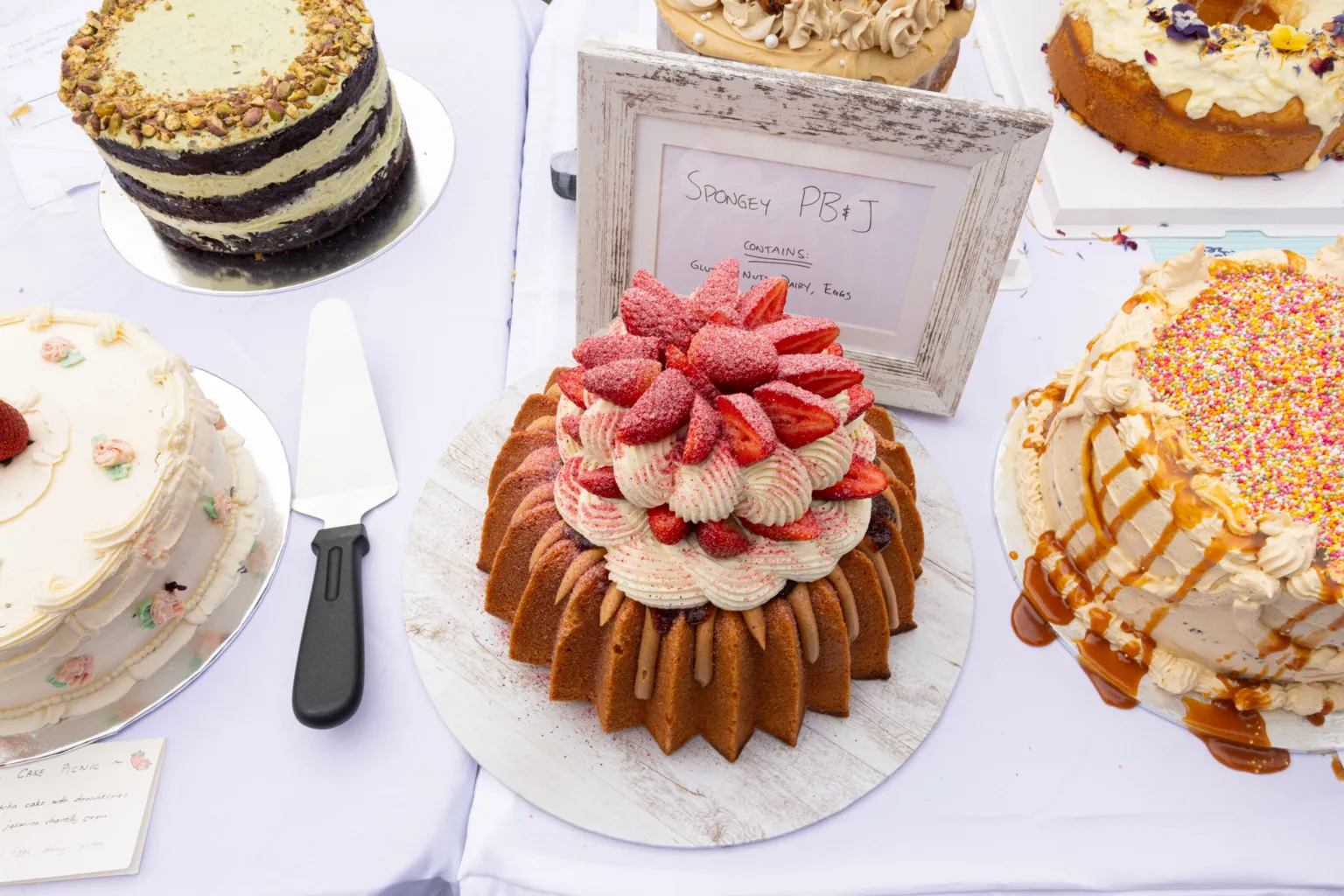 Jessica Hromas/BBC A cream and strawberrry cake (centre) beside a caramel cake with sprinkles on it