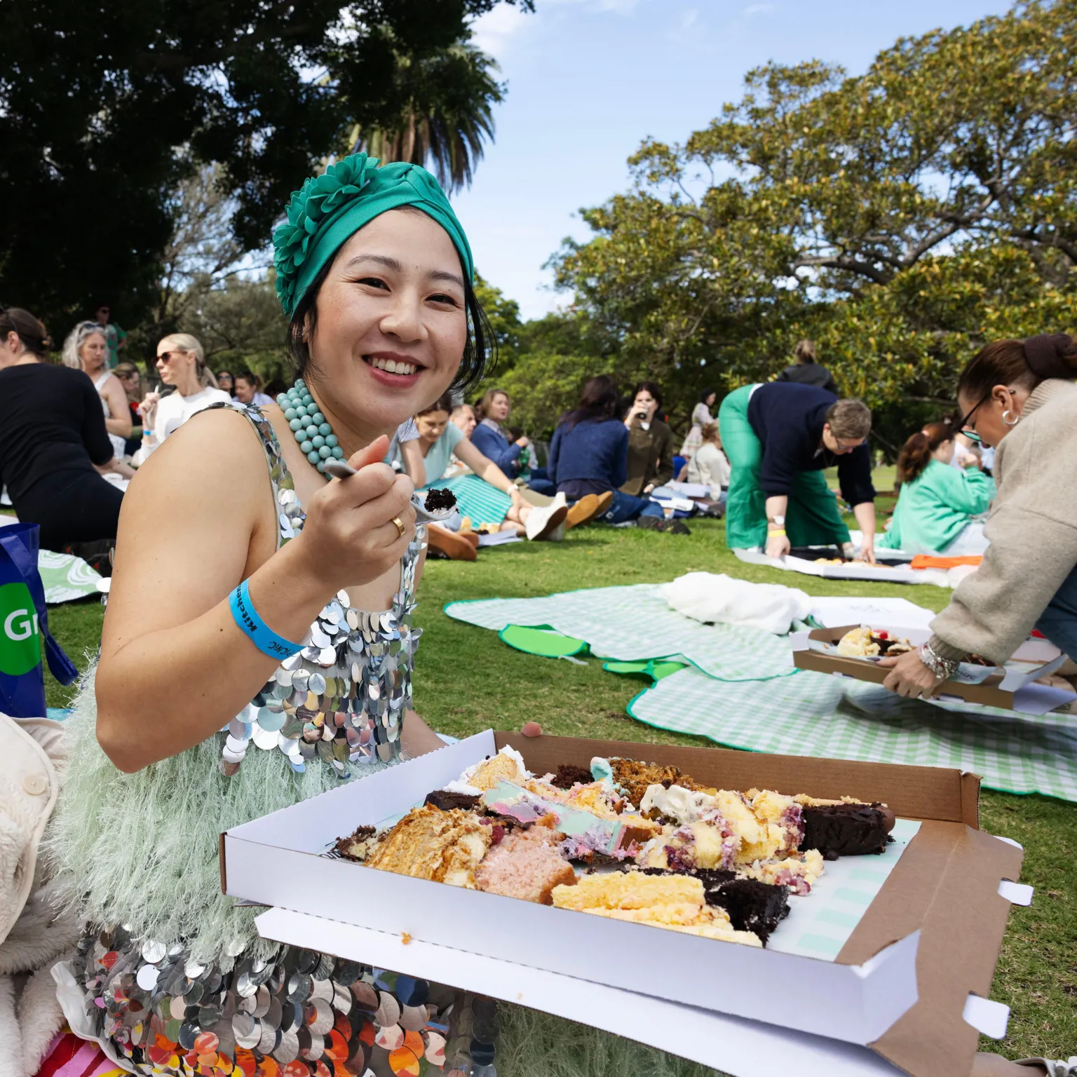 Jessica Hromas/BBC A woman wearing a green headband and a sequined dress, eating cake from a large pizza box with several different slices of cake