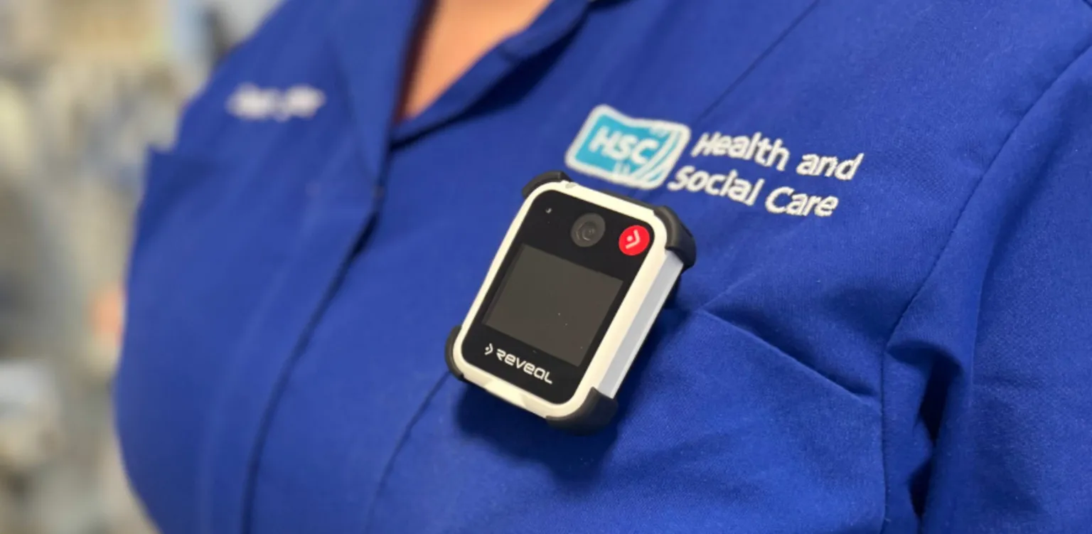 Northern Trust A close-up of a female healthcare worker wearing a body-worn camera on the pocket of her blue tunic