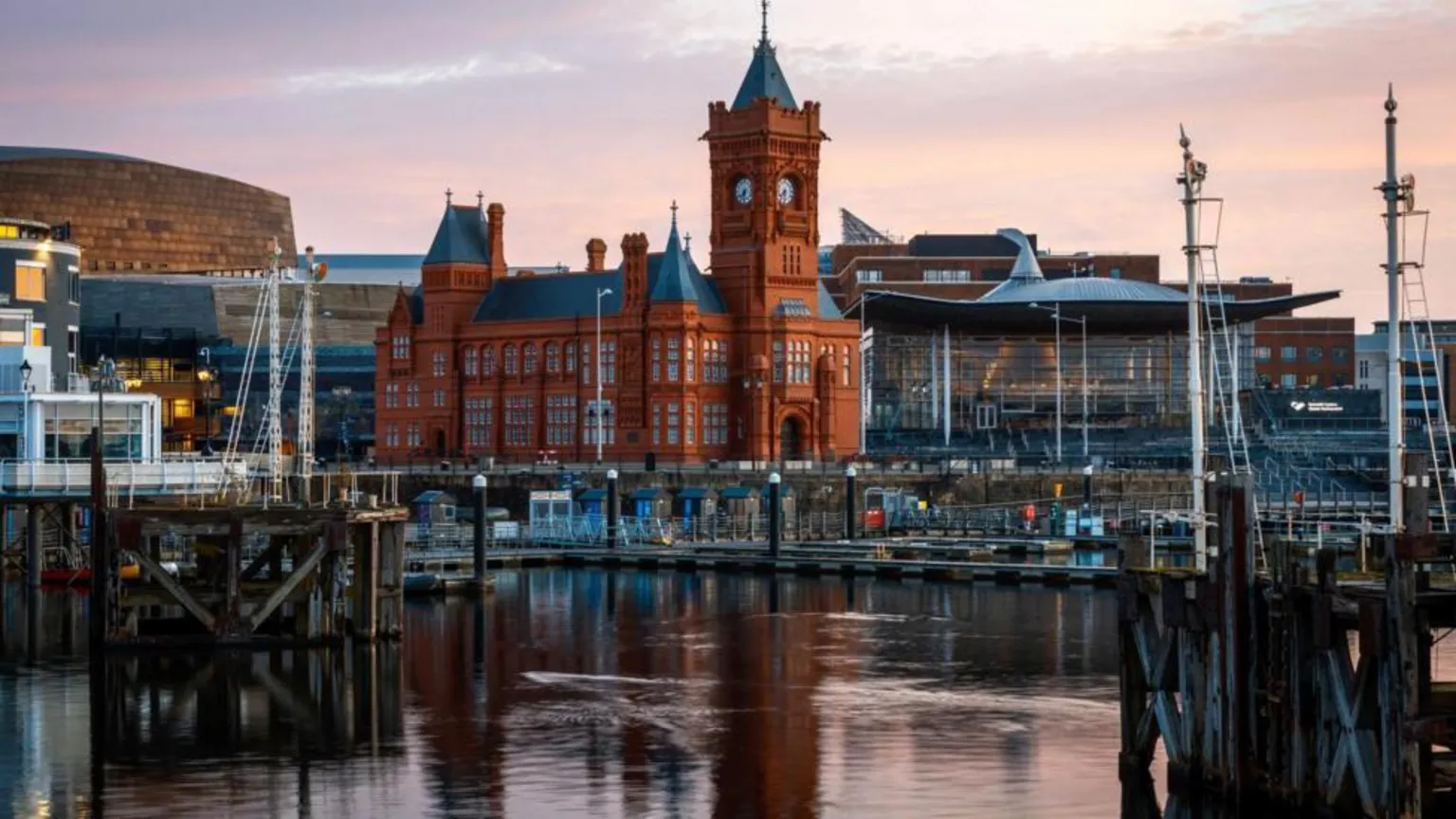  An image of the Senedd building in Cardiff Bay. The Bay's docking platforms are visible in the foreground. The red brick Pierhead building is prominent next to the Senedd. 