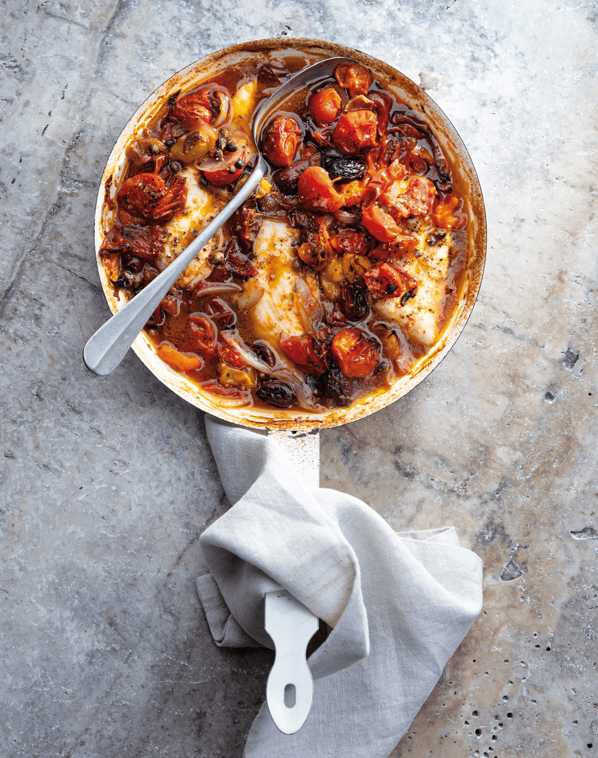 Fish with roasted cherry tomatoes, olives and capers in a serving dish.