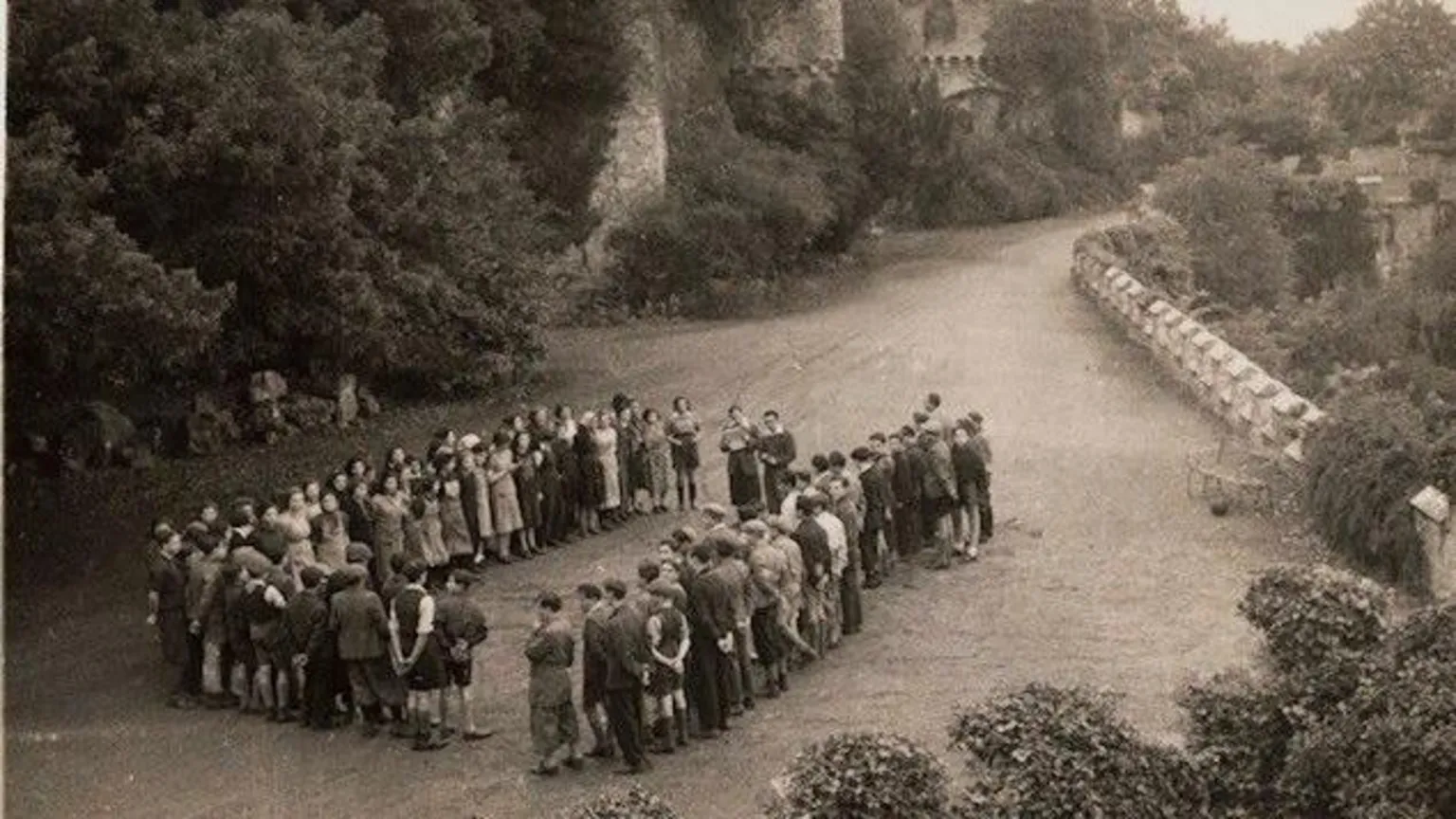 Gwrych Castle Trust Archive Black and white picture of the children on the castle grounds. The group is in the distance, standing in a rectangle.