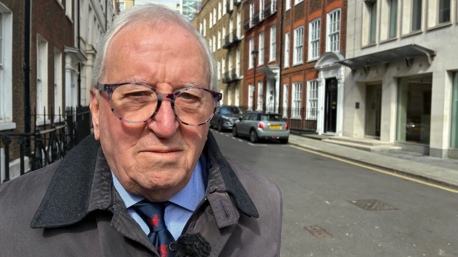 Michael Waller stood wearing a jacket, shirt, and tie in an empty street lined with Georgian buildings