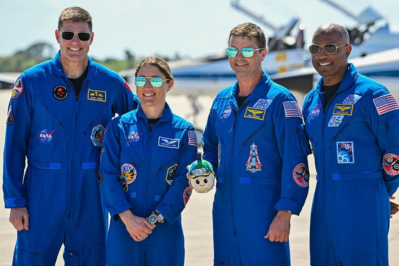 Miguel J. Rodriguez CARRILLO / AFP via Artemis crew stand side by side in blue overalls and sunglasses, smiling at the camera 