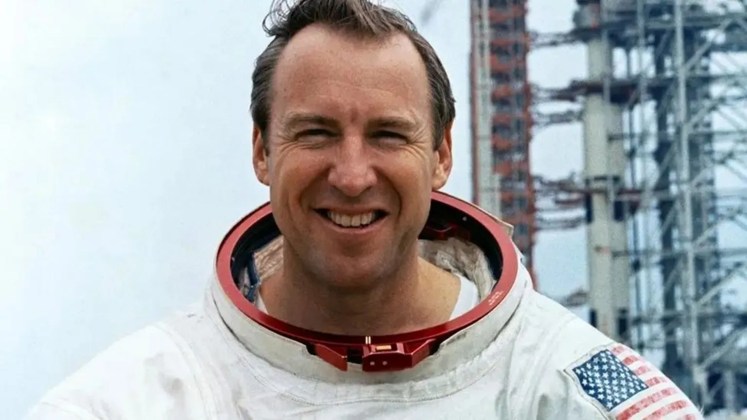 NASA Jim Lovell grins as he stands in front of a launchpad dressed in his spacesuit while training for the Apollo 13 mission