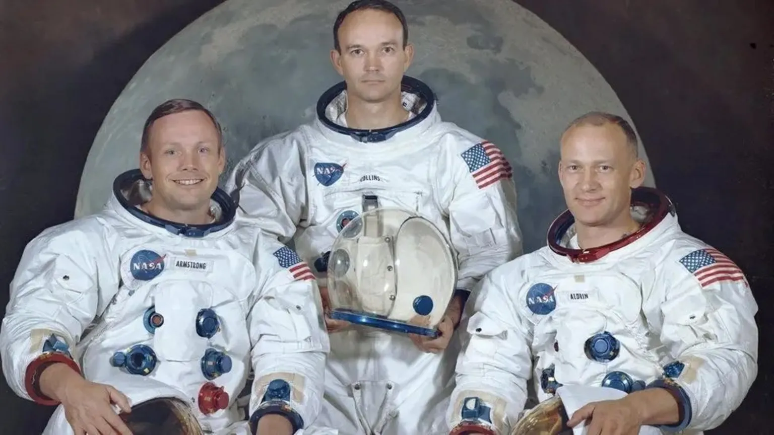 NASA Official portrait of the Apollo 11 crew Neil Armstrong, Michael Collins and Buzz Aldrin, dressed in their spacesuits, taken against the backdrop of an image of the Moon