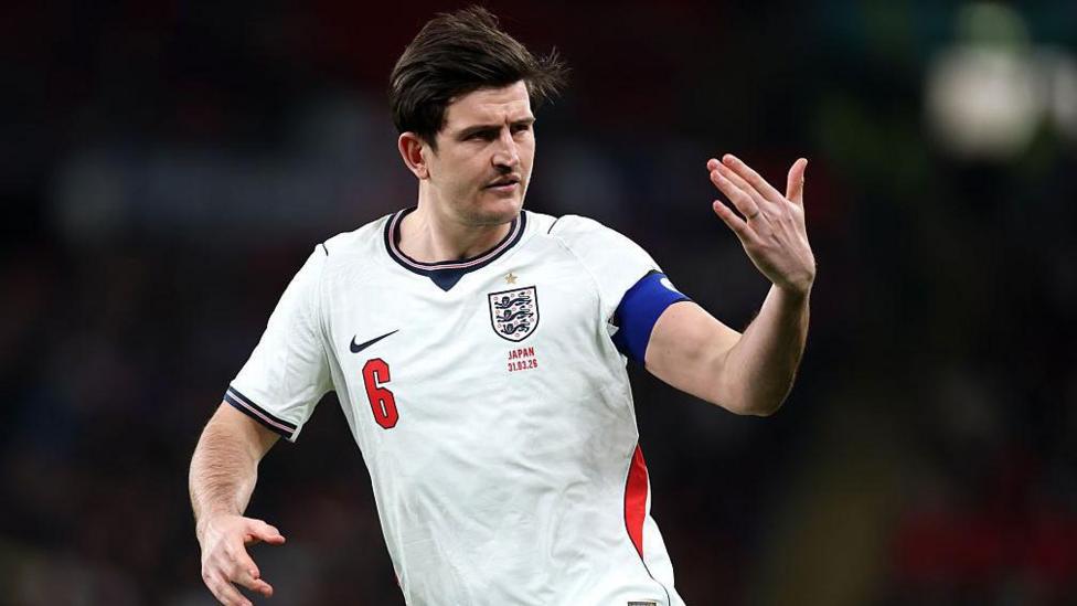 Harry Maguire makes a sign with his left hand while playing in England's white shirt during the game against Japan